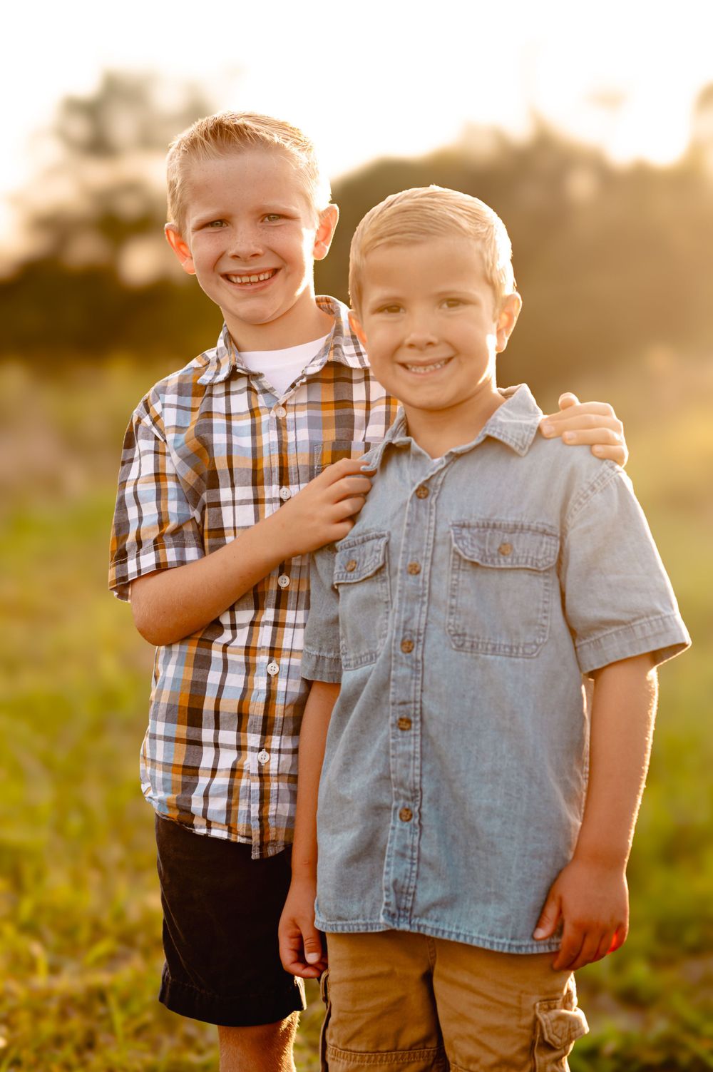 Two happy children in casual button-down shirts smiling together outdoors during golden hour.