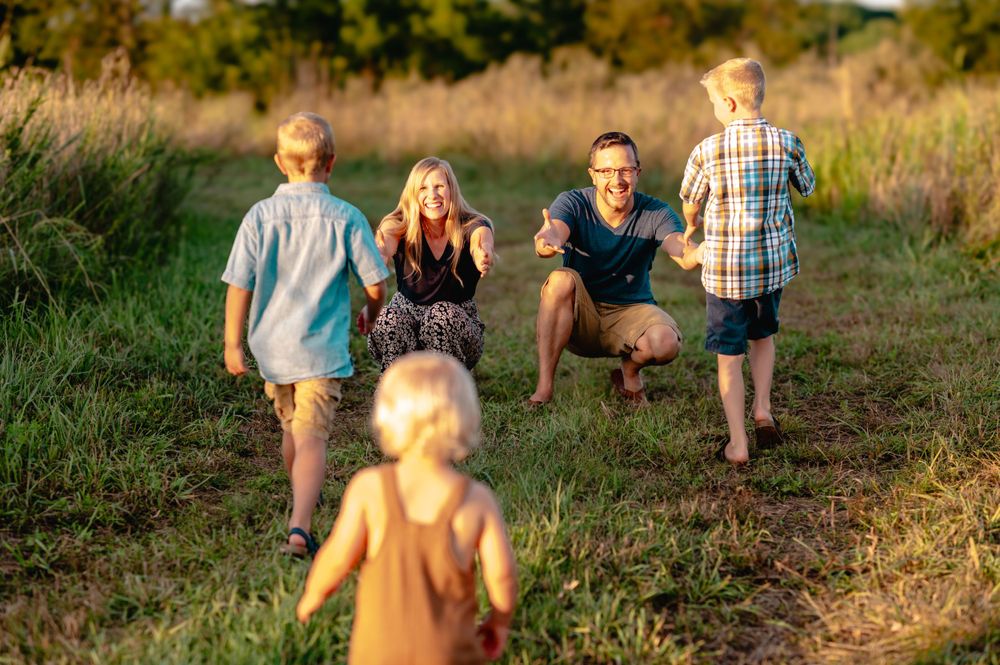 Playful family moment outdoors with children running through a sunlit meadow at golden hour.