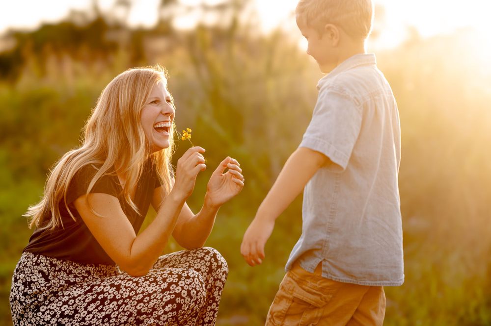 A candid moment between two people laughing together in a sunlit field during golden hour.