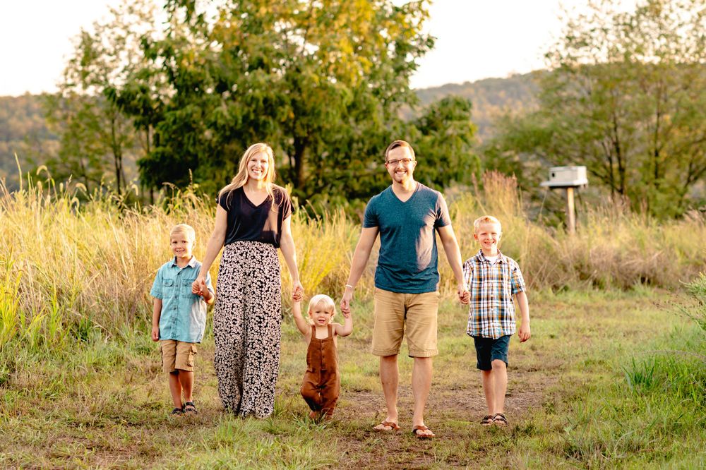 A family standing together in a field with tall golden grass and autumn trees behind them.