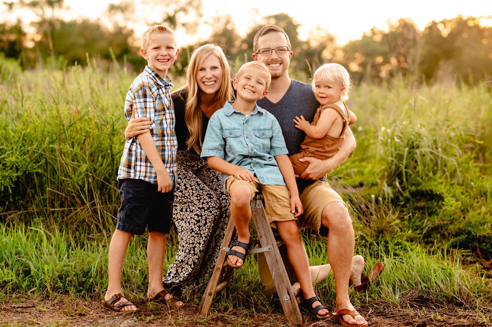 A group poses together in a grassy field during golden hour sunset with warm lighting and natural scenery.