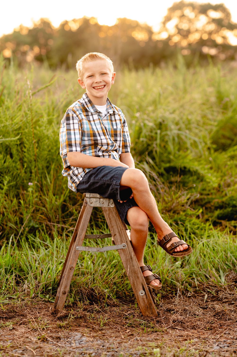 Outdoor portrait of someone sitting on a wooden stool in a plaid shirt and shorts during golden hour.