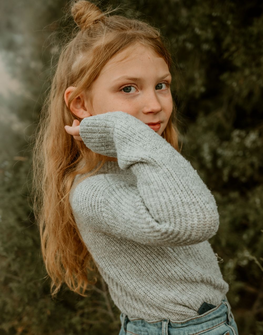 Child in gray sweater making playful expressions in outdoor portrait series.