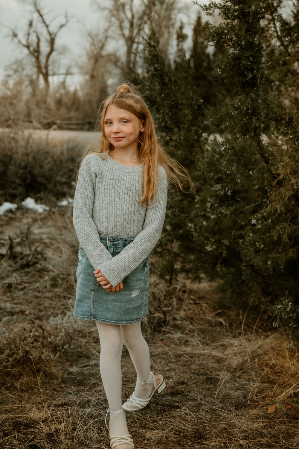 Child in gray sweater and denim playing outdoors in autumn setting.