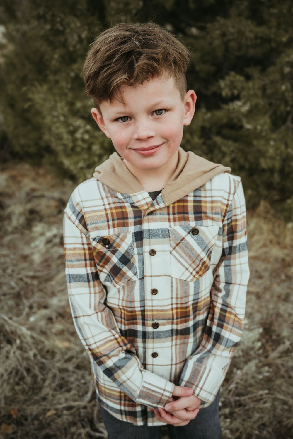 Child wearing plaid button-up shirt smiles during outdoor portrait session.