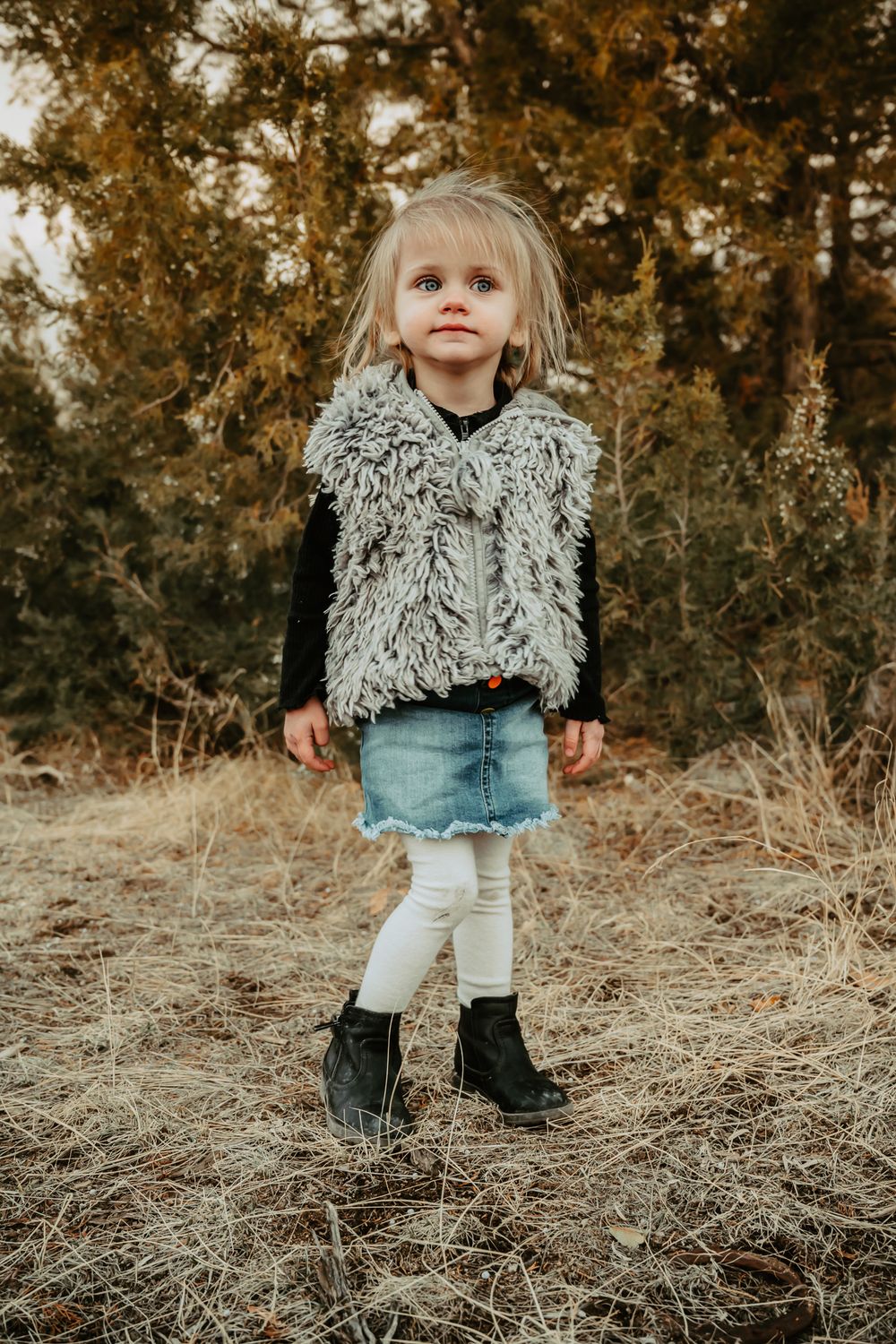 Toddler in stylish winter outfit explores natural outdoor setting during photo session.