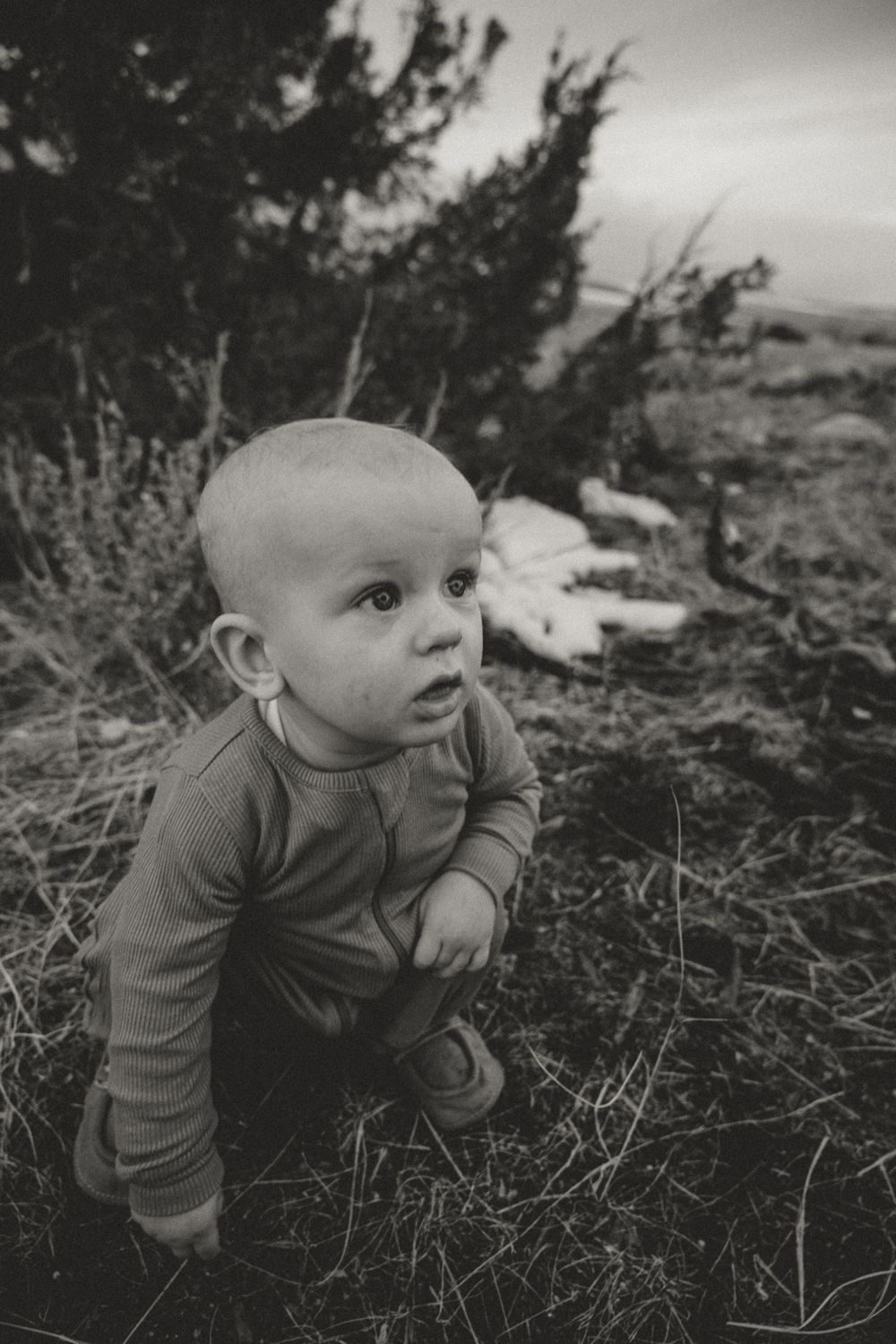 Baby in gray outfit crawling on ground in black and white photo.