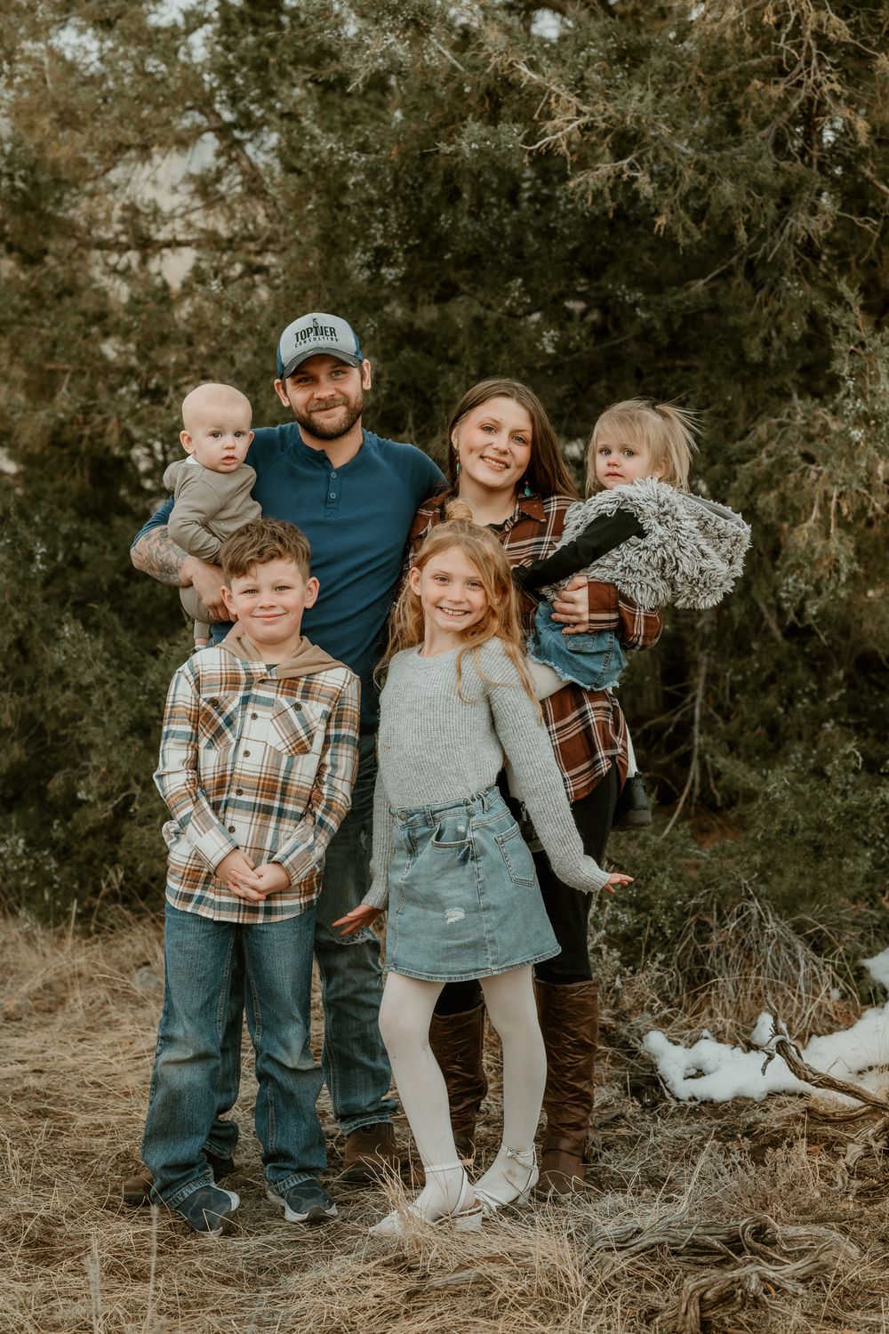 Family group smiling and posing together in outdoor setting with natural backdrop.