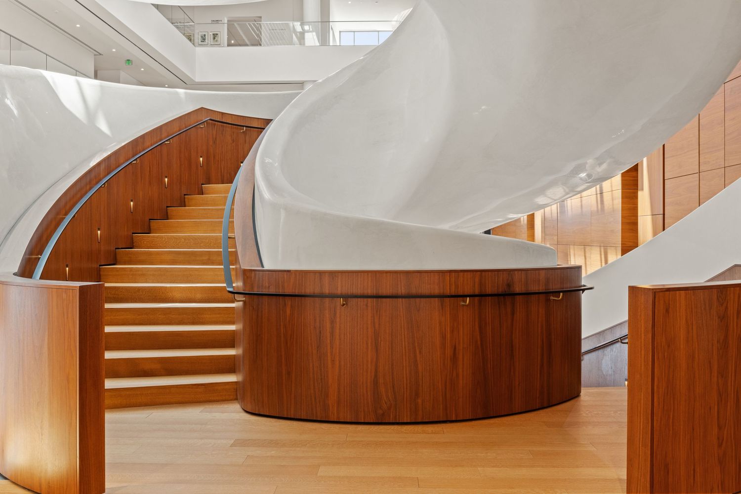 Modern curved wooden staircase with glass railing and white walls creates an elegant architectural statement in interior space.