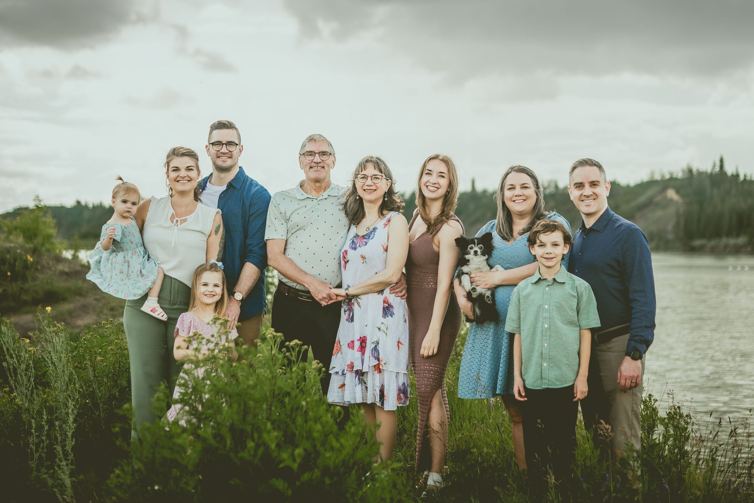 Extended family poses together for outdoor portraits near a lake on an overcast day.