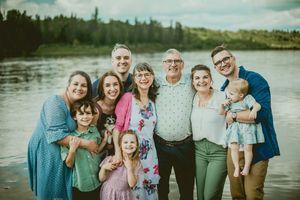Extended family group poses together by a lakeside on a summer evening wearing coordinated blue and pink outfits.