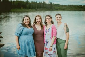 Group of friends posing together by a serene lake with trees in background at sunset.