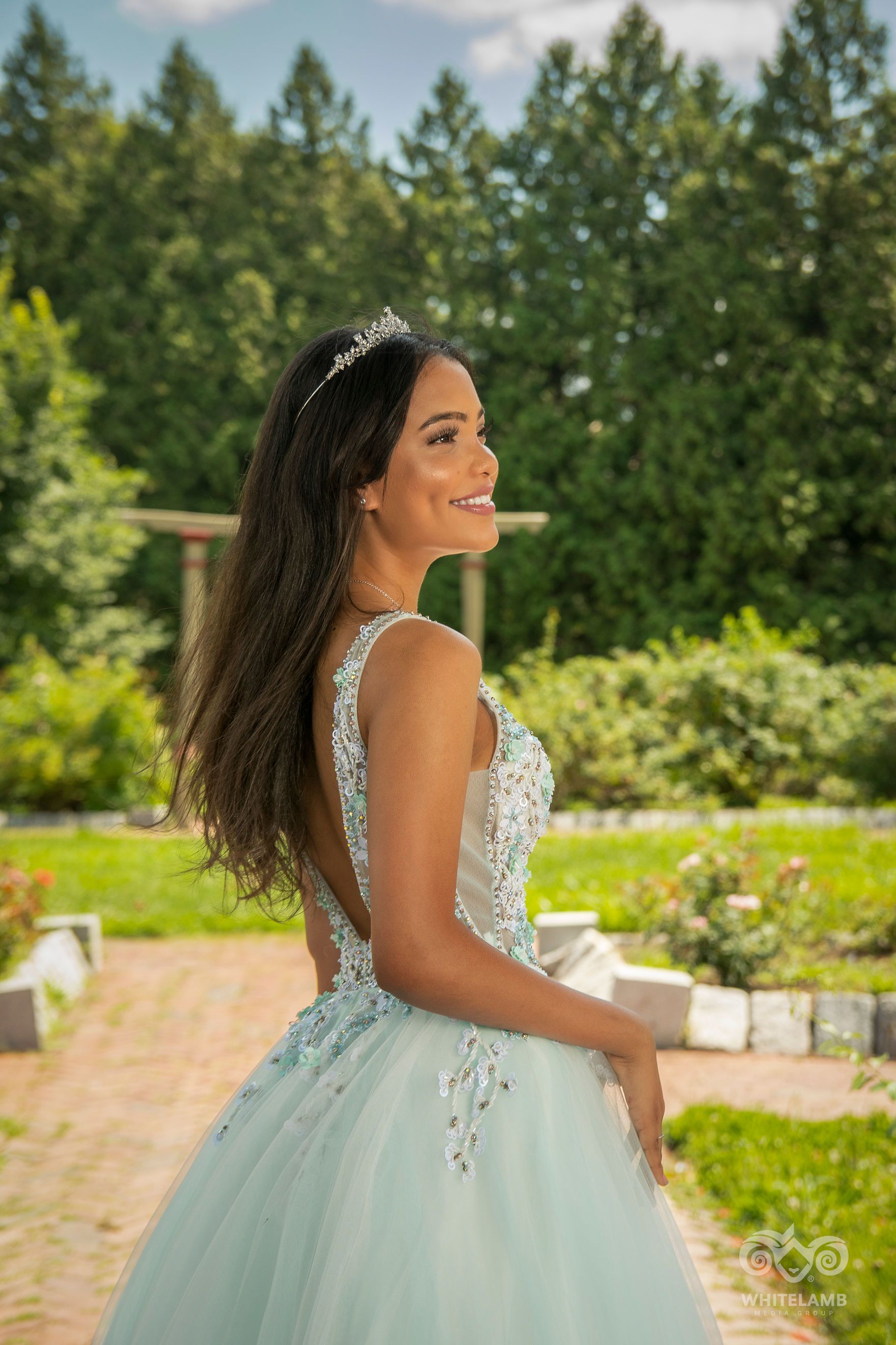 Beautiful light blue quinceanera dress worn in an outdoor garden setting with pine trees in the background.