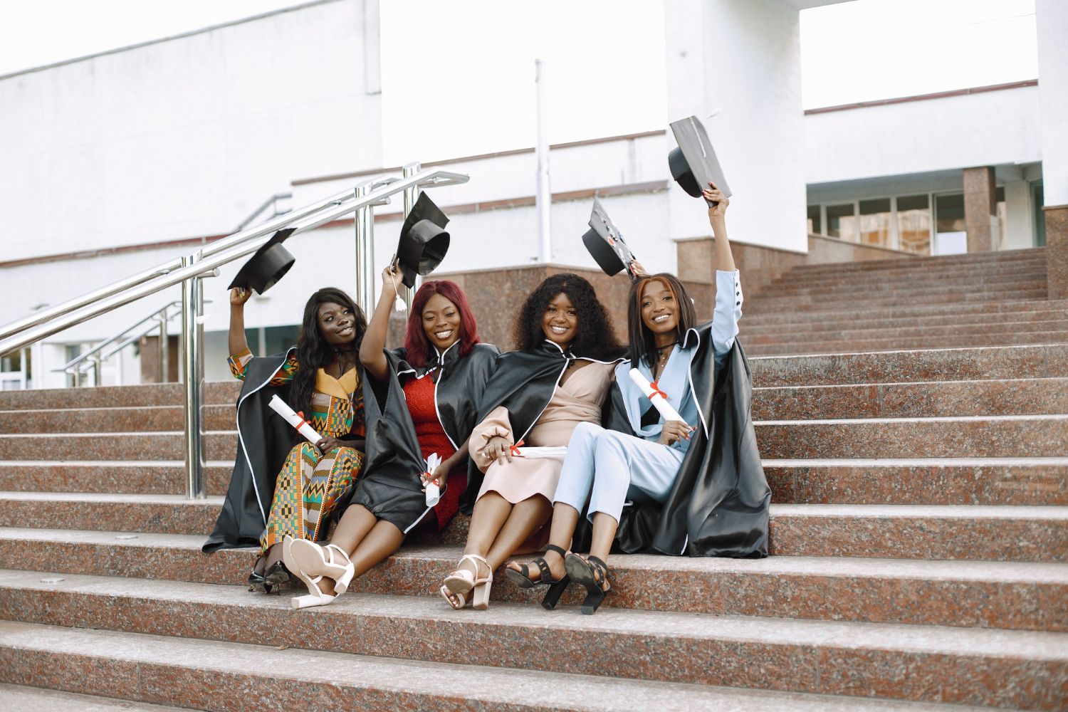 Graduates in academic regalia celebrate on concrete steps while holding their diplomas.