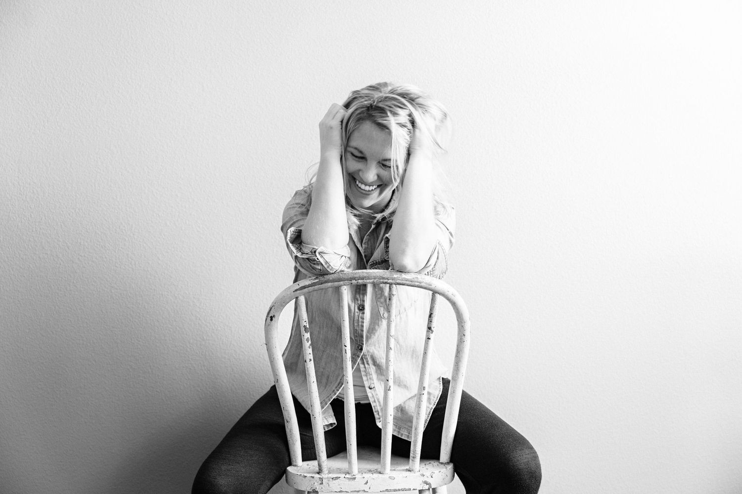 Black and white photo of lifestyle photographer Kasha Gage sitting on a chair and laughing in Orange County studio.
