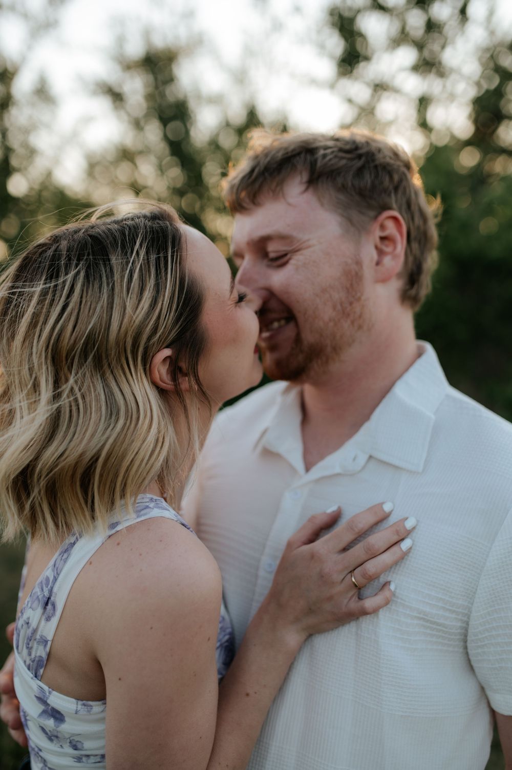 A romantic couple shares intimate kisses while embracing outdoors during sunset photography session.