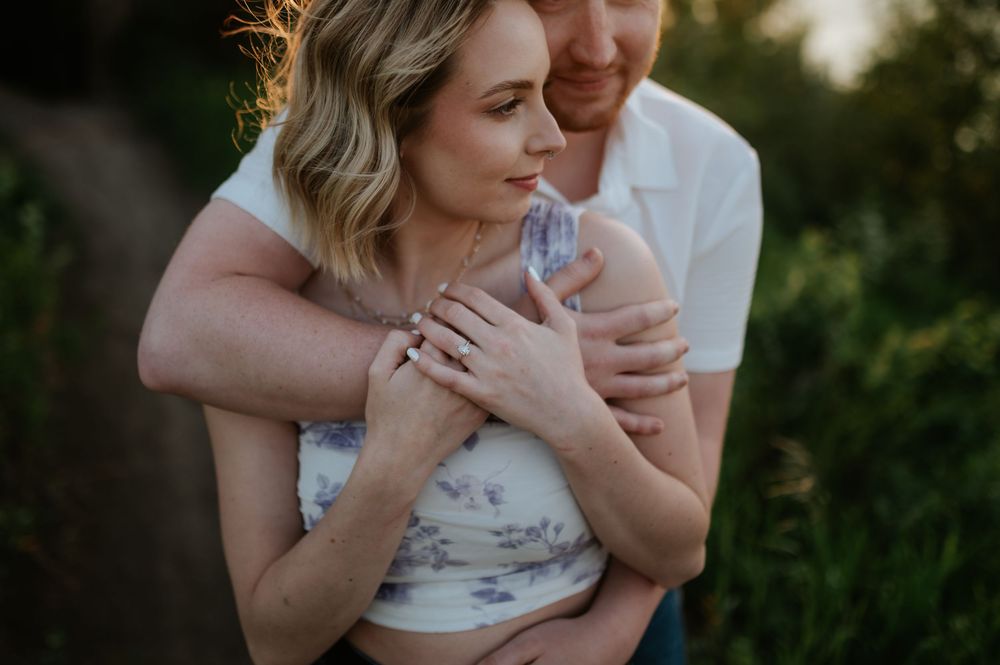 Couple embraces tenderly in a romantic outdoor golden hour photoshoot with greenery in background.