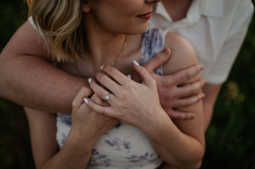 Close up shot showing crossed hands with an engagement ring in soft natural lighting against floral fabric.