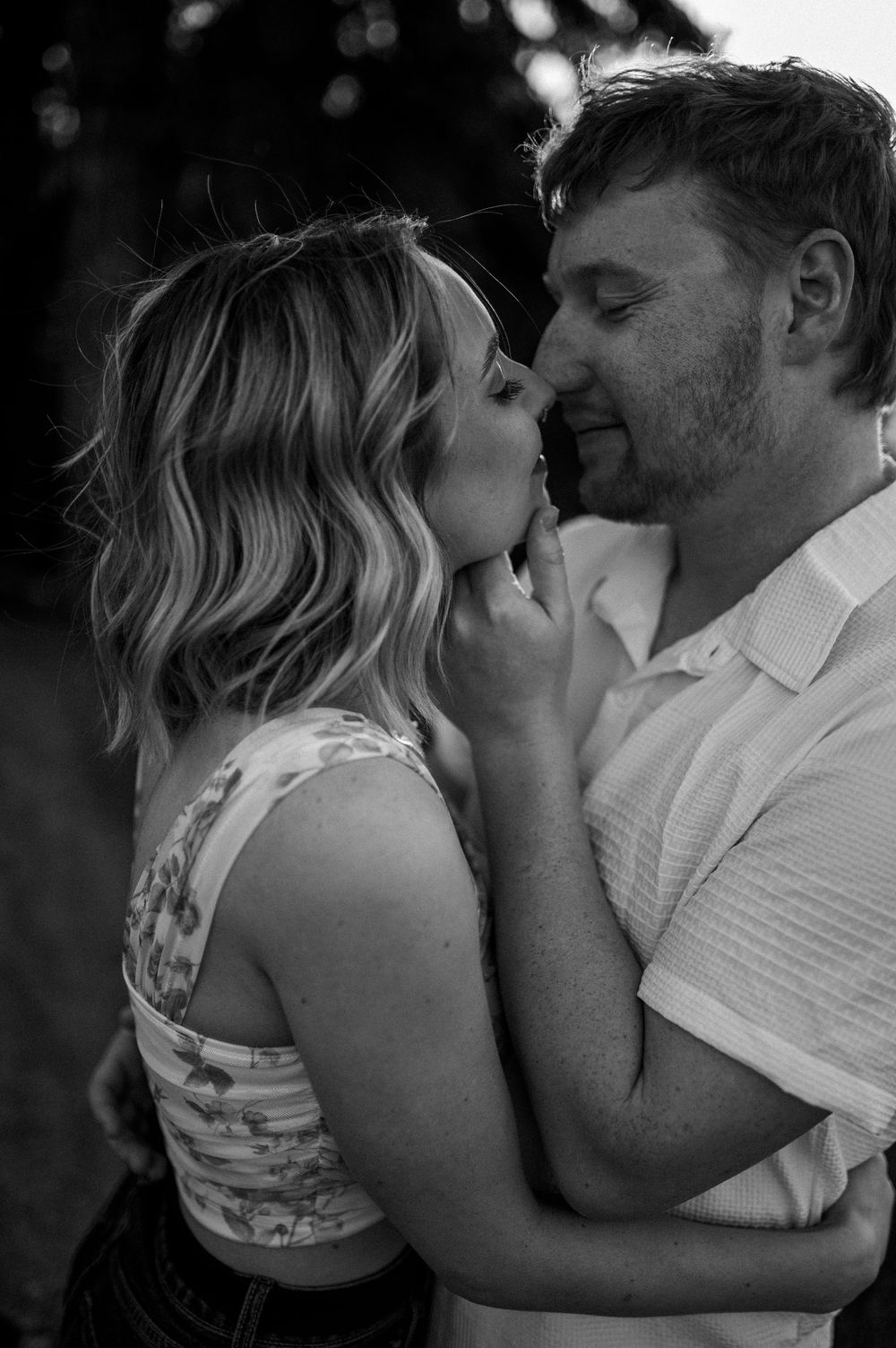 Black and white romantic portrait of a couple sharing an intimate moment outdoors in casual summer attire.