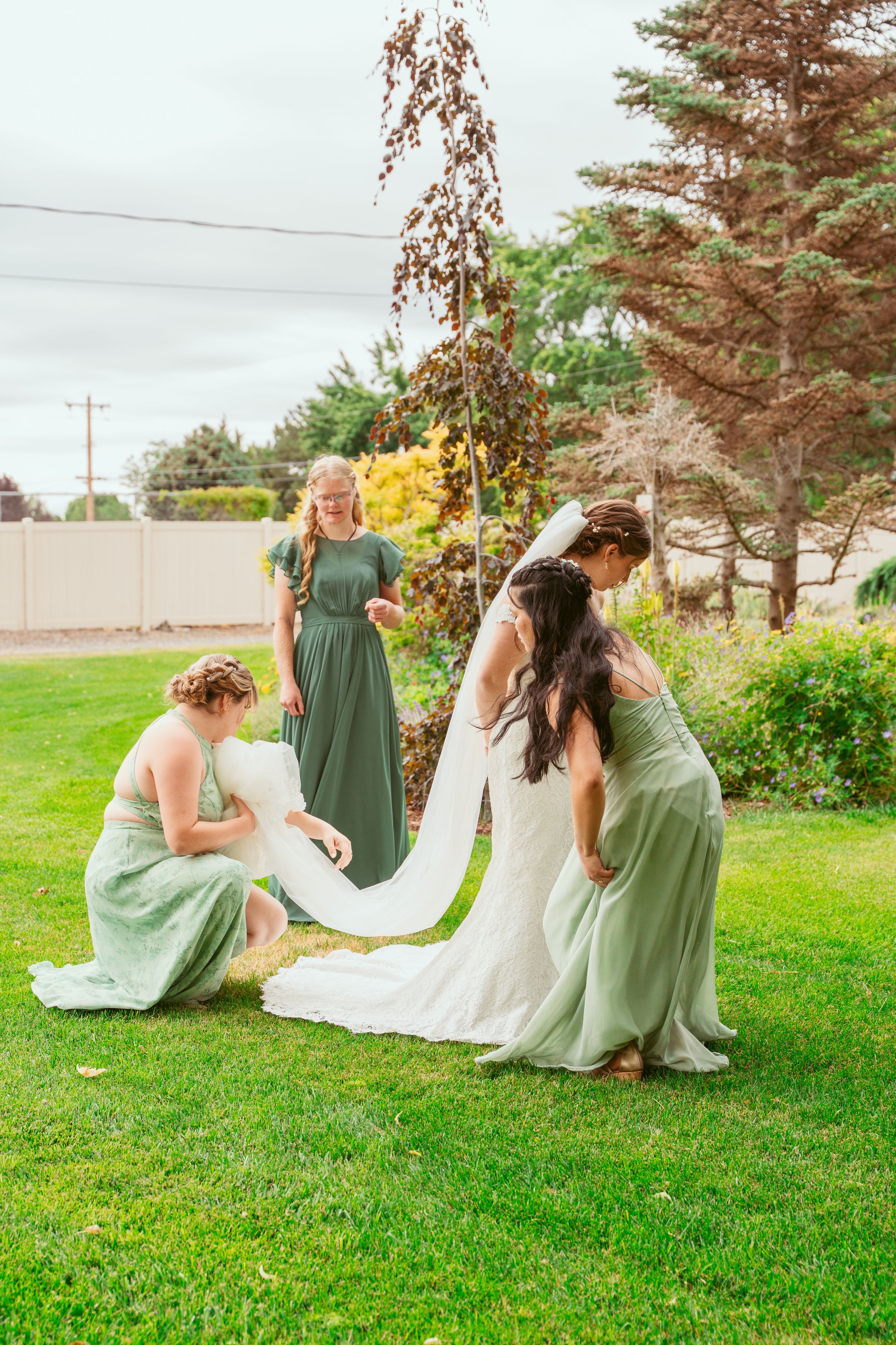 Three figures in sage green and white dresses lounge together on a lush green lawn during a summer event.