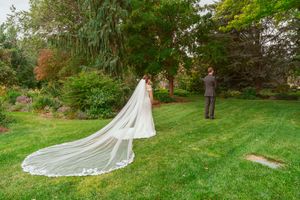 Wedding couple meets for their first look on a lush green lawn with a dramatic cathedral-length veil trailing behind.