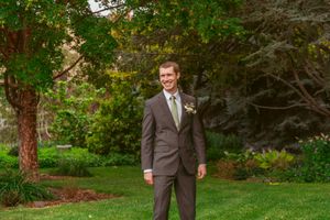 A group of groomsmen in gray suits walk through a lush garden path during a wedding.