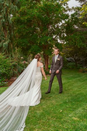 A couple shares a romantic moment in a garden setting with a dramatic flowing veil trailing behind the bride's gown.