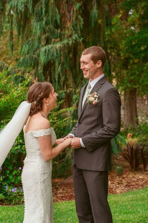 A joyful wedding couple shares a candid moment together outdoors with lush greenery and willow trees in the background.