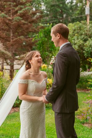 A joyful wedding moment captured between a bride in an off-shoulder dress and groom in a garden setting.