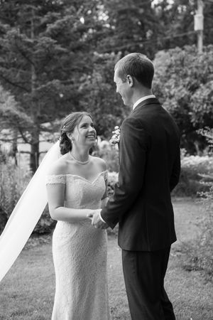 Black and white photo of a bride and groom sharing a delightful moment during their wedding ceremony outdoors.