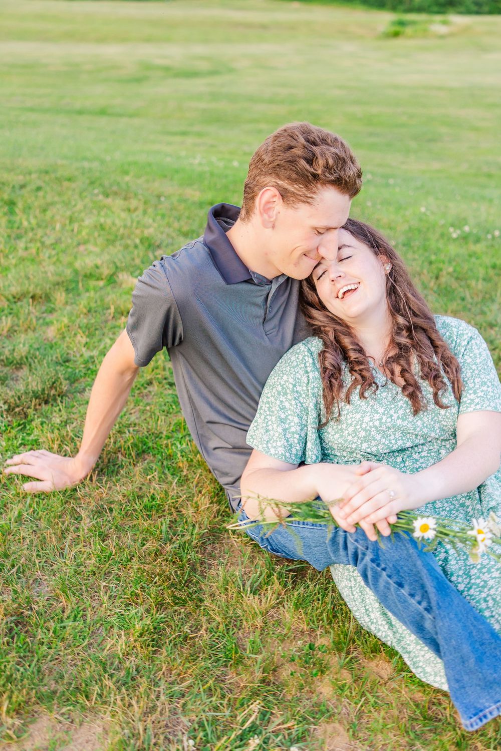 A joyful couple laying in the grass outdoors sharing a playful and candid moment together.