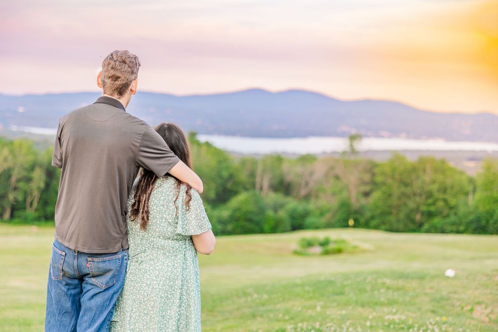A couple enjoying a sunset walk on a grassy hillside with mountains in the background.