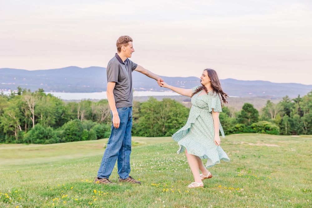 A couple in casual attire holds hands while walking through a scenic mountain meadow on a summer afternoon.