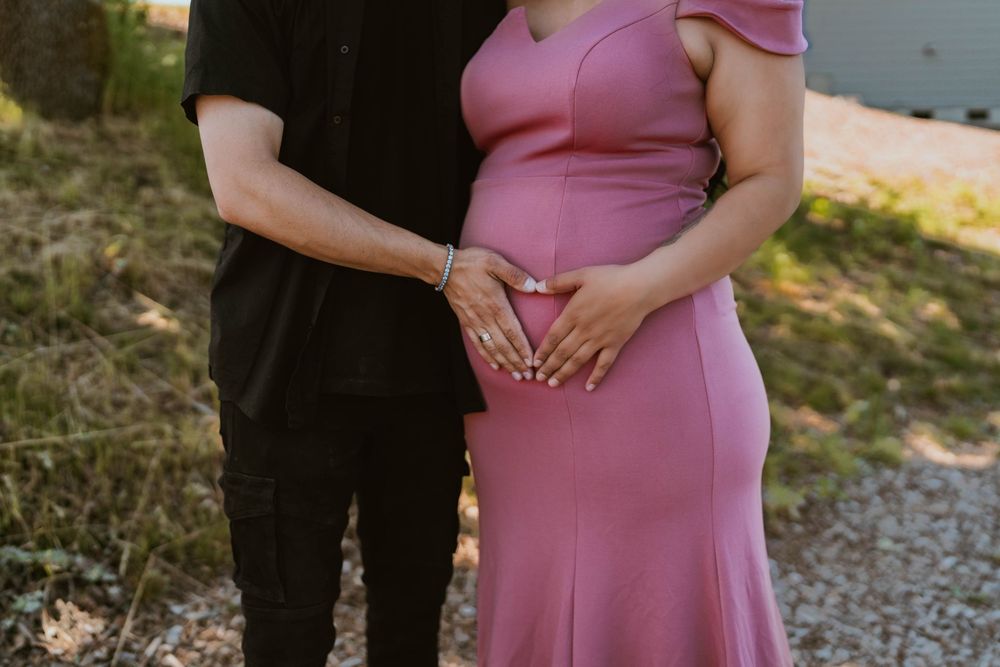 Couple forming a heart shape with hands over pregnant belly in pink dress.