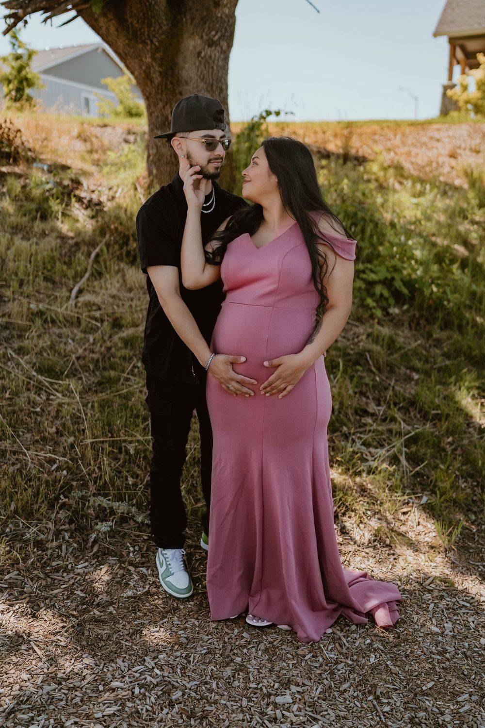 Expecting couple sharing a tender moment outdoors, woman in pink maternity gown.