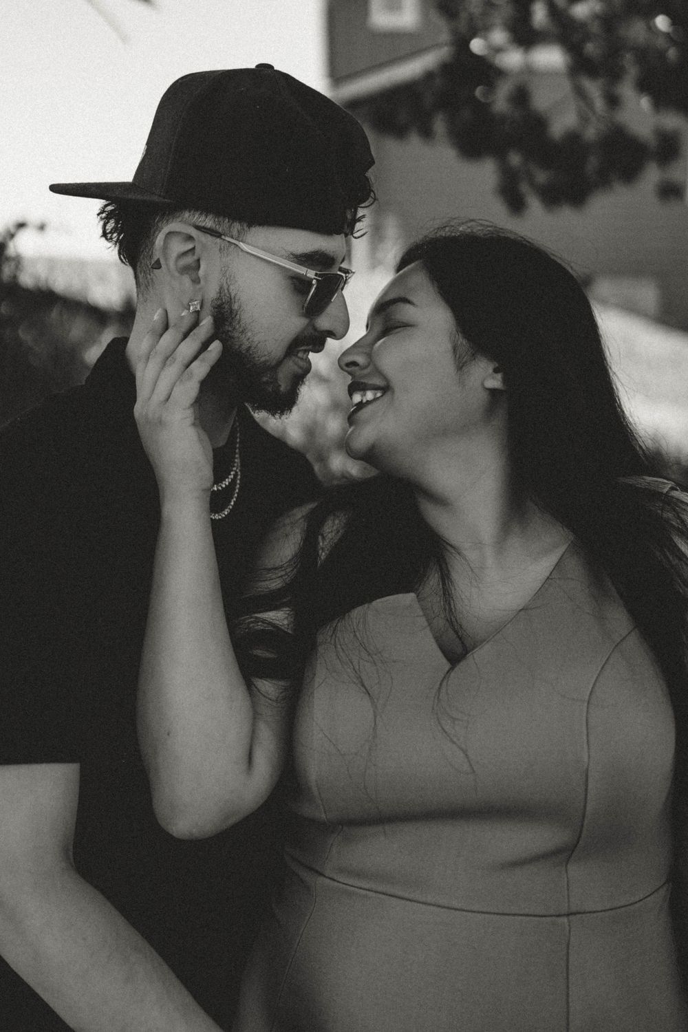 Black and white close-up of a laughing pregnant couple about to kiss outdoors.