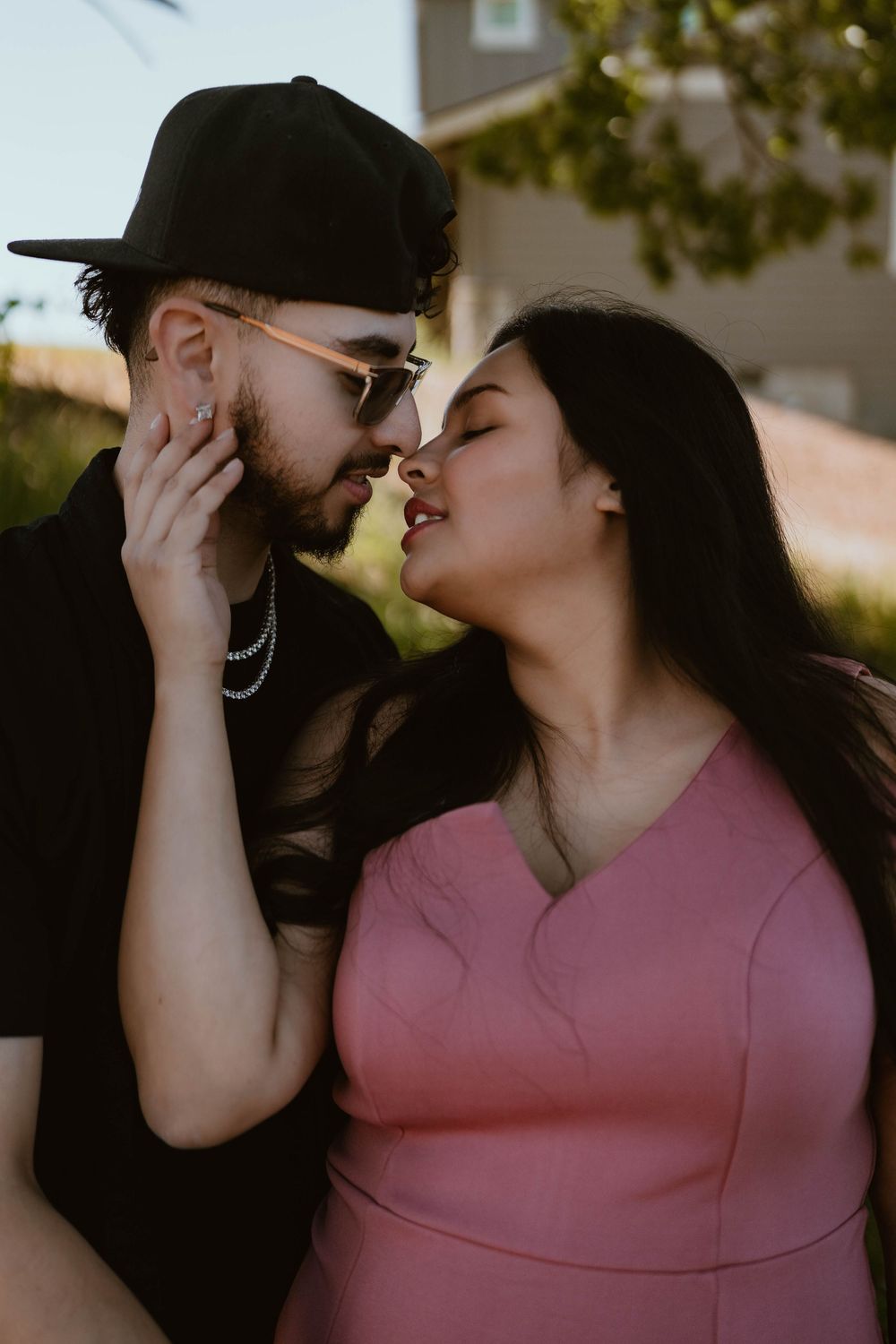 Couple sharing a romantic almost-kiss outdoors, woman in pink dress, man in black.