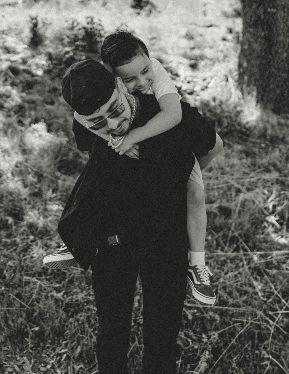 Black and white photo of a father giving his young son a piggyback ride outdoors.