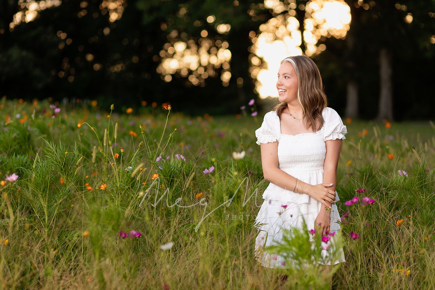 A white-dressed teen stands peacefully in a sunlit wildflower meadow at golden hour. Senior pictures with MegMc Photography, Medina, TN