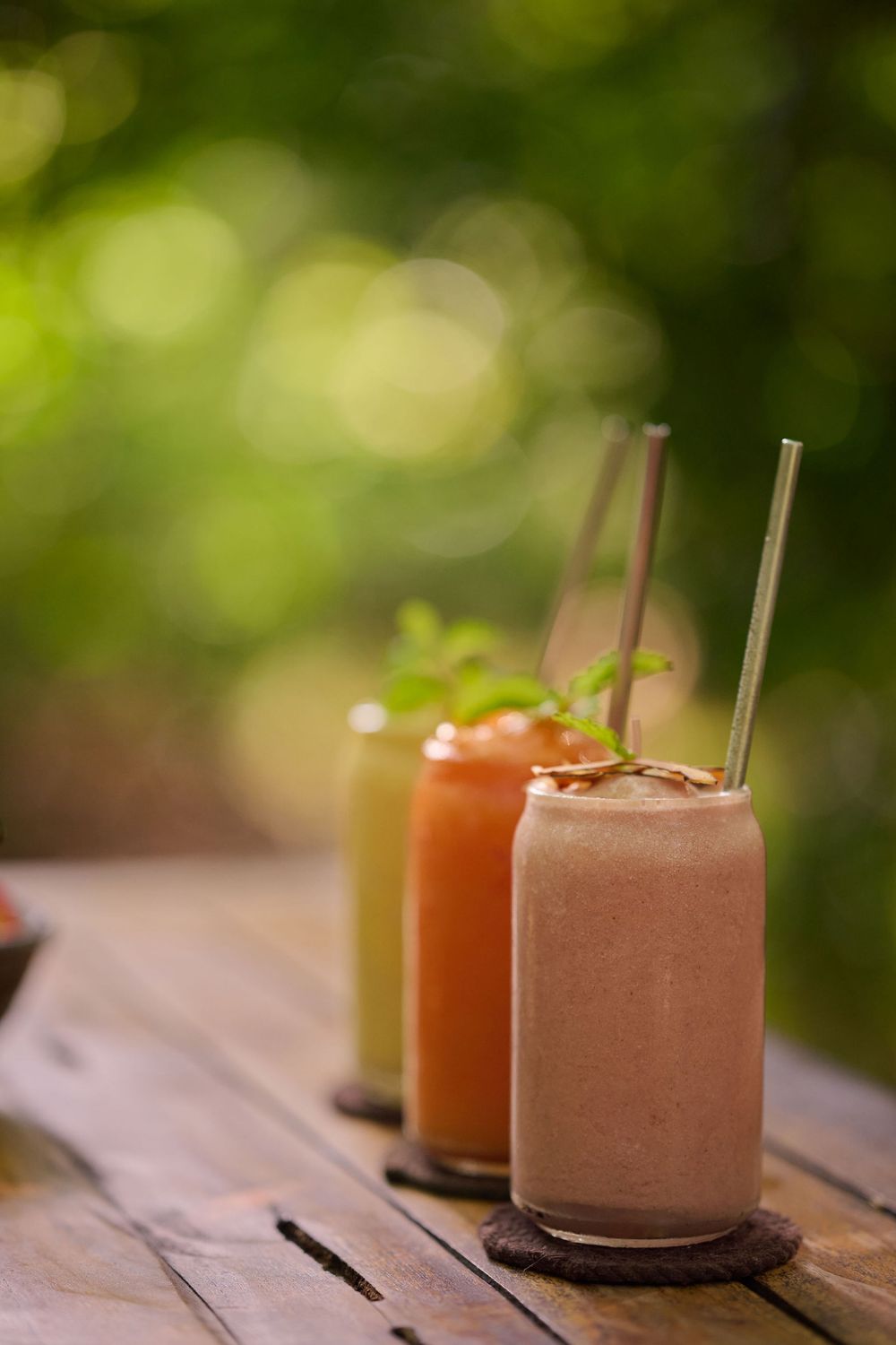 Three creamy milkshakes with chocolate and strawberry flavors garnished with whipped cream sit on a wooden table outdoors.