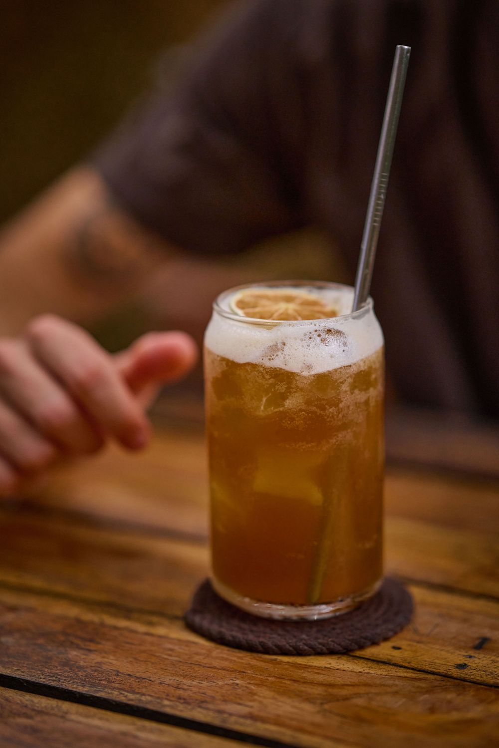 Several craft cocktails in rustic glasses sit on a wooden surface with amber-colored liquid and foam on top.