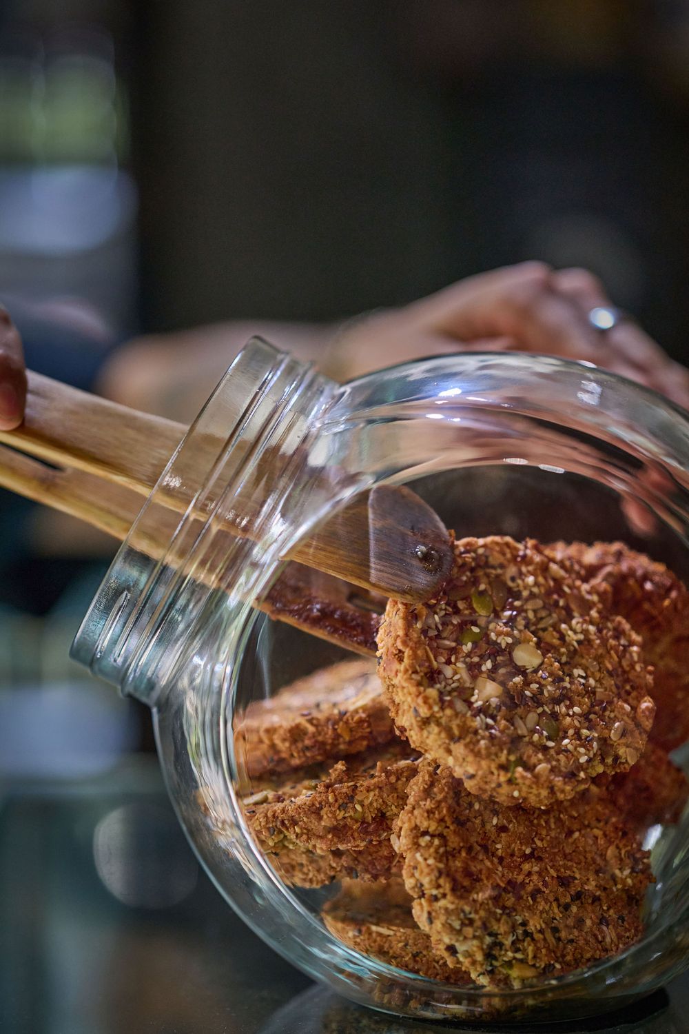 Homemade cookies with nuts and seeds spilling out of a glass cookie jar.