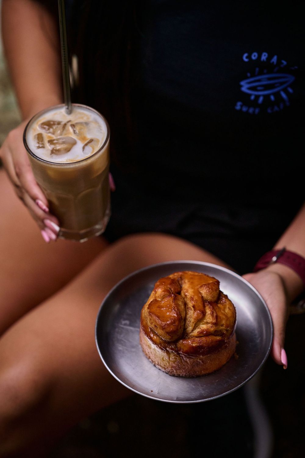 Iced coffee and a gourmet pastry served on a metal plate in moody lighting.