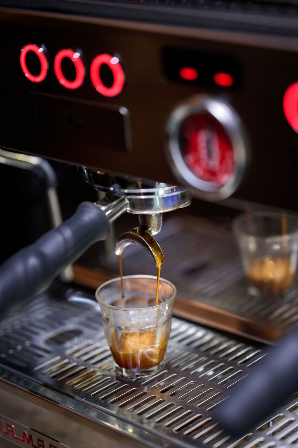 Espresso shot being pulled from a professional coffee machine with red digital display.