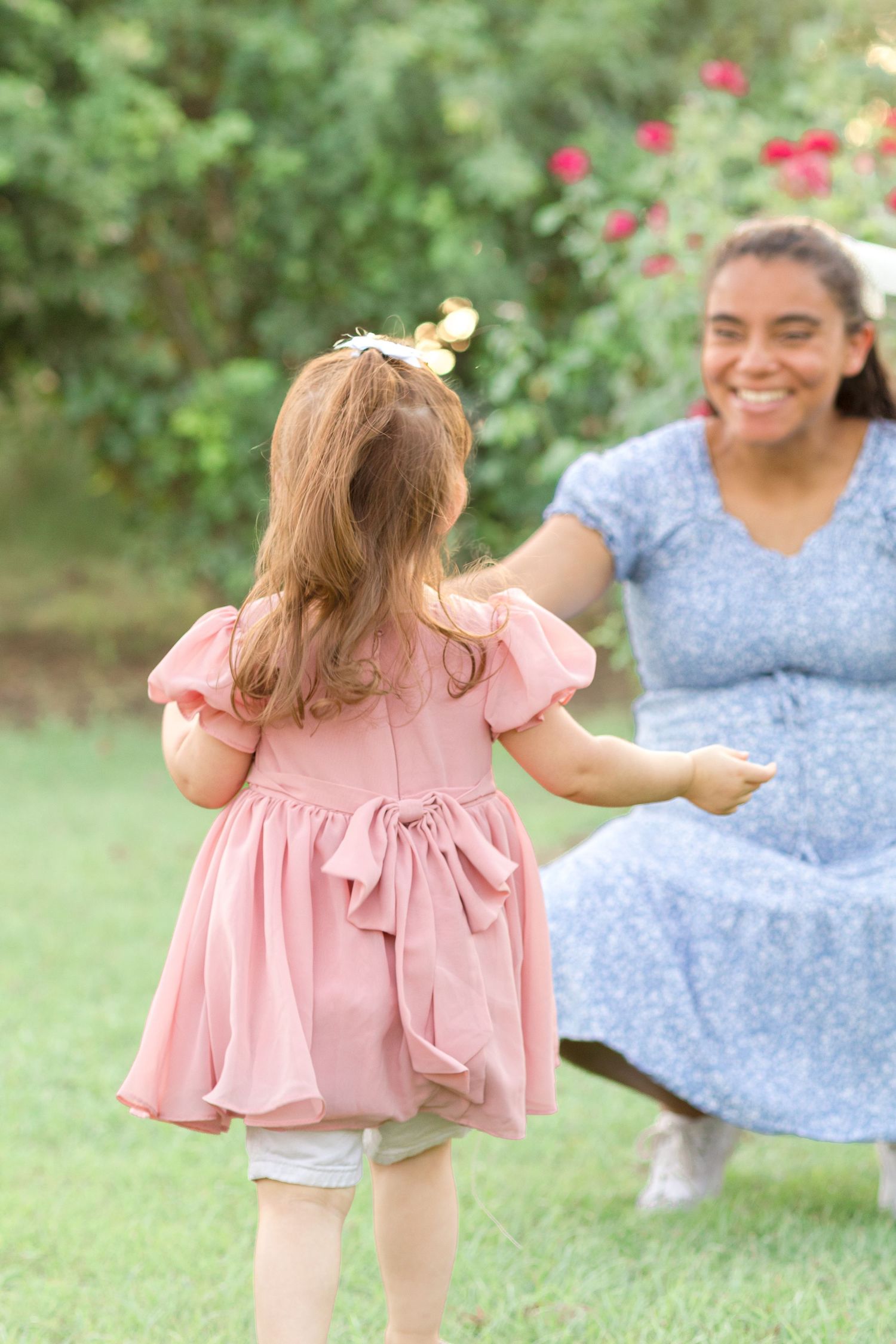 Toddler girl running towards mom who is bent down opening arms ready to embrace daughter in a garden in Mesa, Arizona.