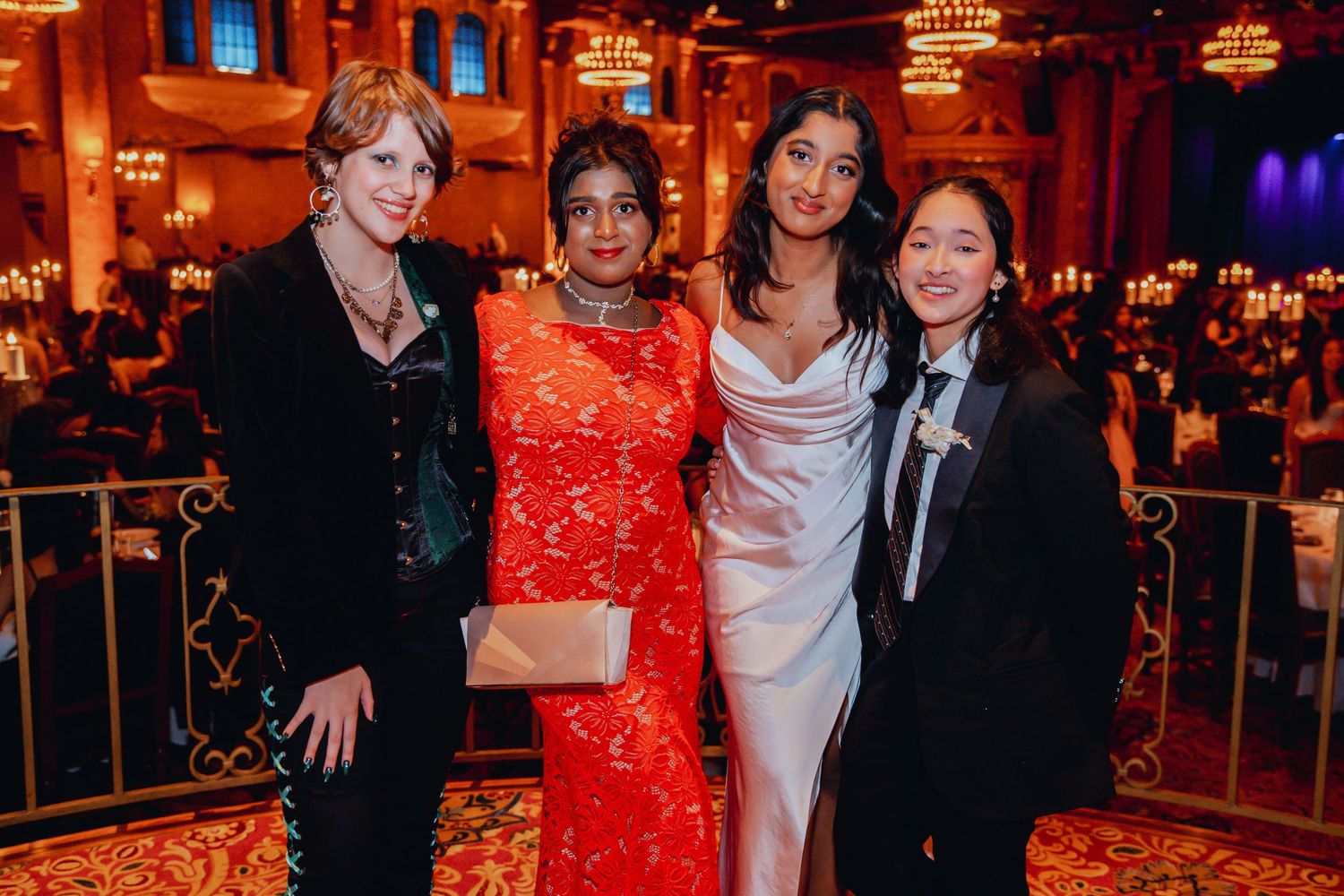 Four people in elegant evening attire pose together at a formal gala event with chandeliers and ambient lighting.