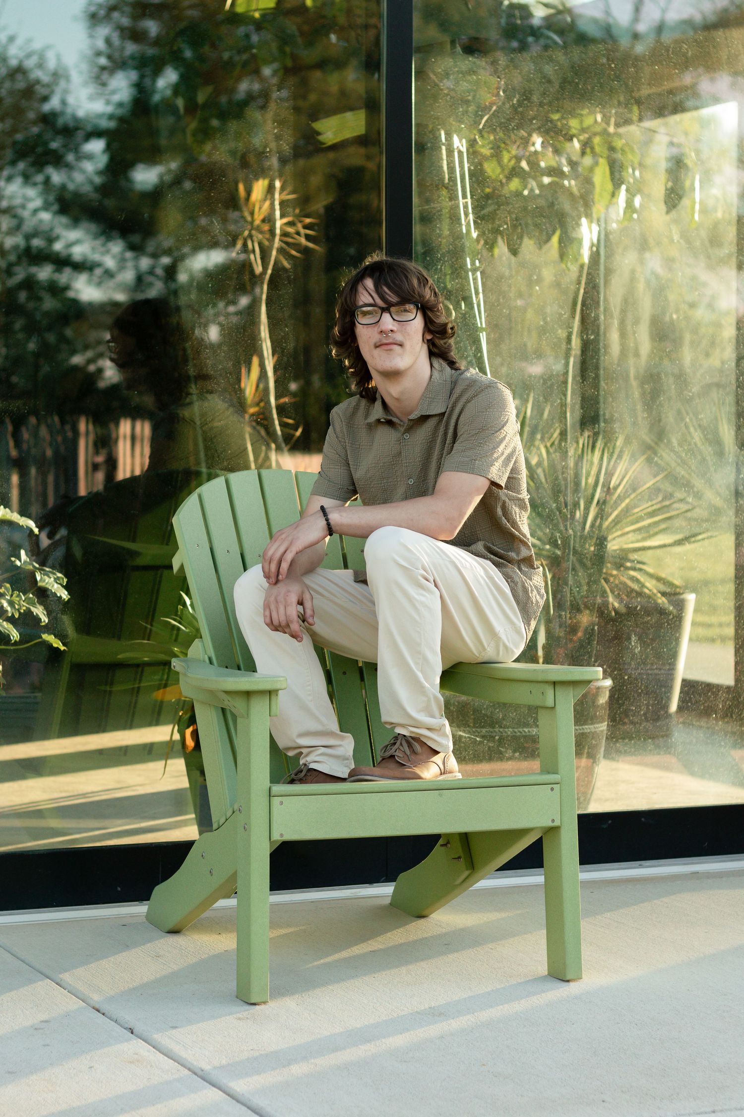 A person in casual attire relaxing on a mint green Adirondack chair on a sunlit porch.
