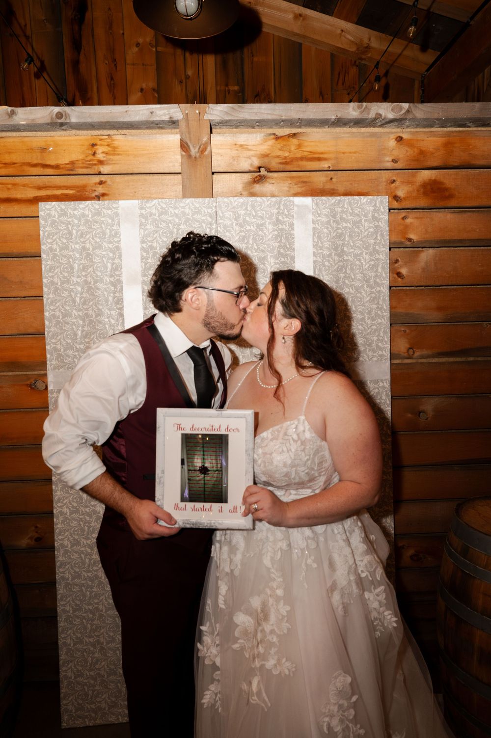 Four romantic wedding photos show a couple in a rustic wooden venue sharing kisses and holding a frame.