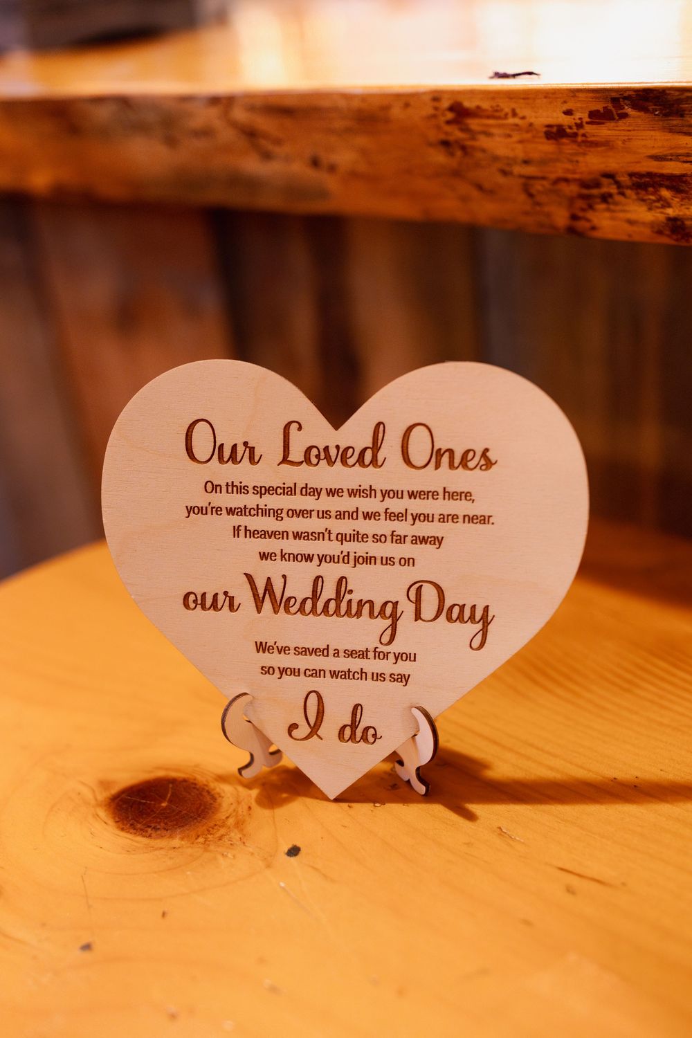 Heart-shaped wedding memorial sign reading 'Our Loved Ones' on rustic wooden surface in warm lighting.