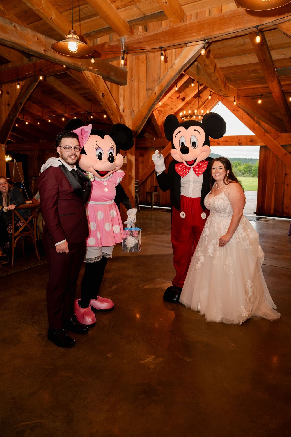 Mickey and Minnie Mouse characters pose with a couple in formal attire at a rustic barn wedding reception venue.